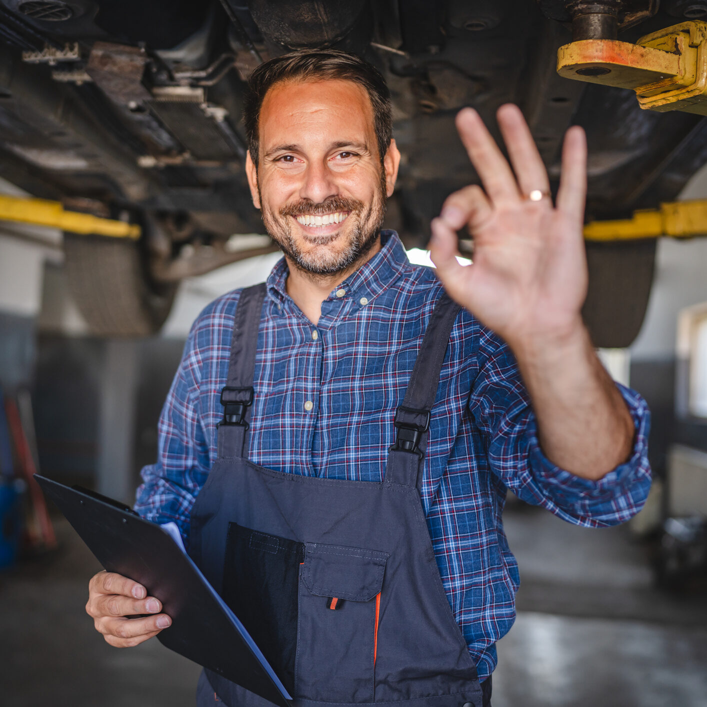Car mechanic making okay gesture under the car with friendly smile